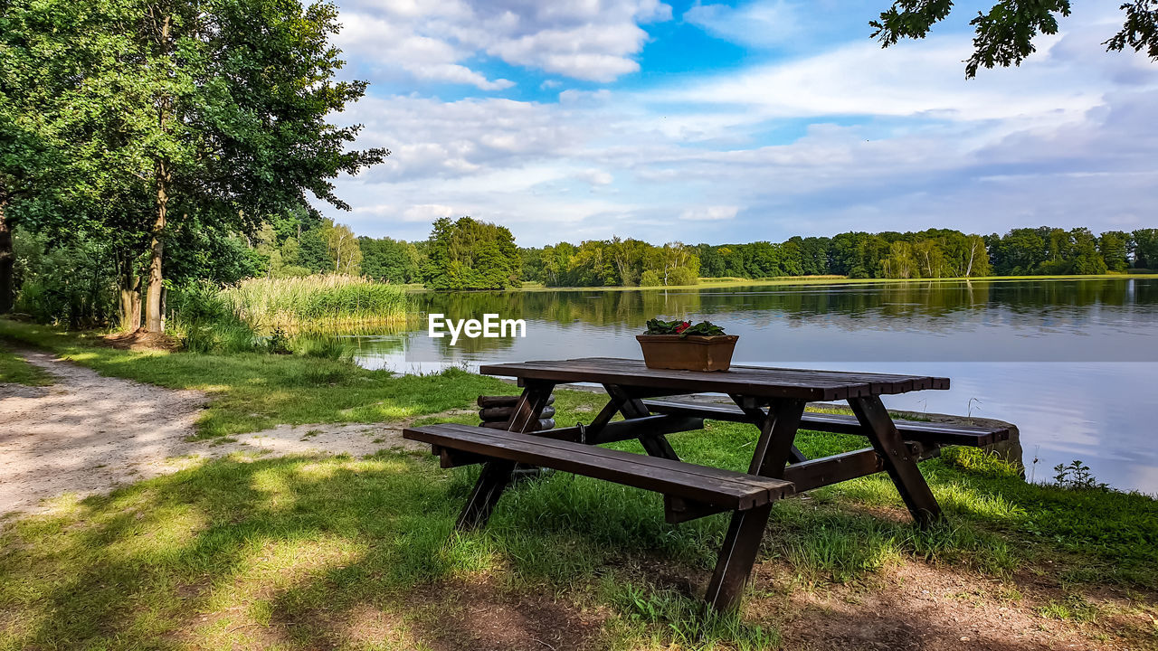 EMPTY CHAIRS AND TABLE AGAINST TREES AT LAKE