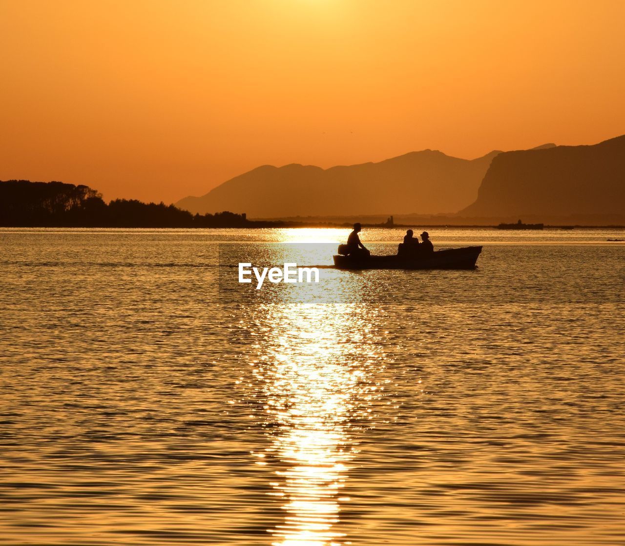 Silhouette people sailing on boat in river against clear sky during sunset