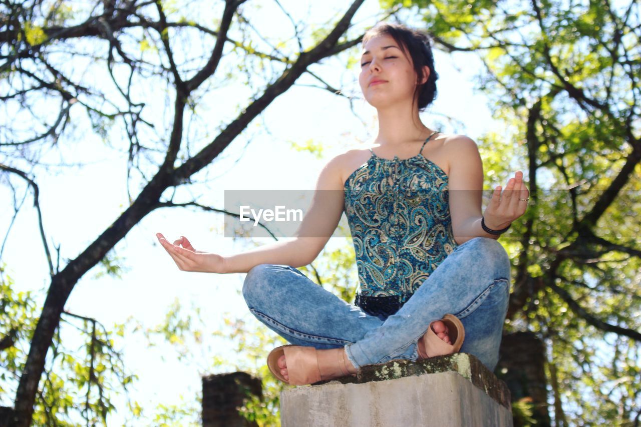 Low angle view of teenage girl meditating against sky