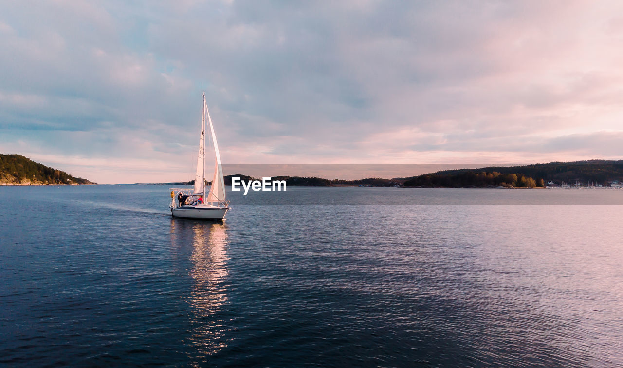 SAILBOAT SAILING IN SEA AGAINST SKY DURING SUNSET