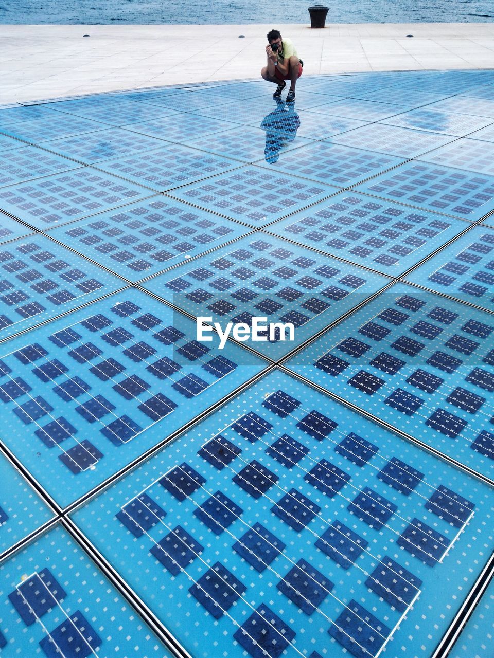 Full length of man photographing while crouching on tiled floor against sea