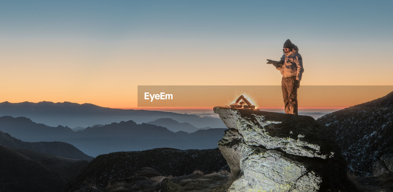 Scenic view of man standing on landscape against sky during sunset