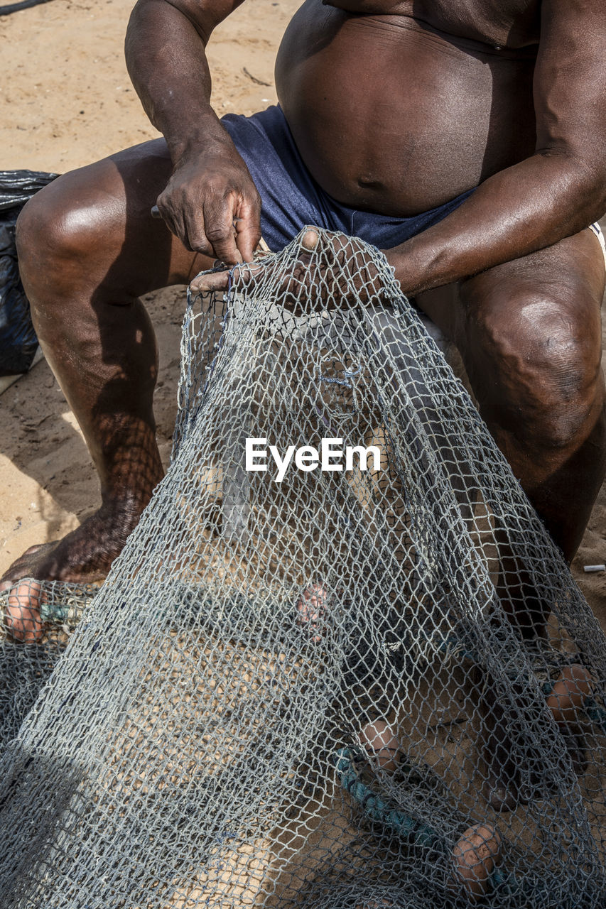 Fisherman repairing fishing net after a period of heavy use.