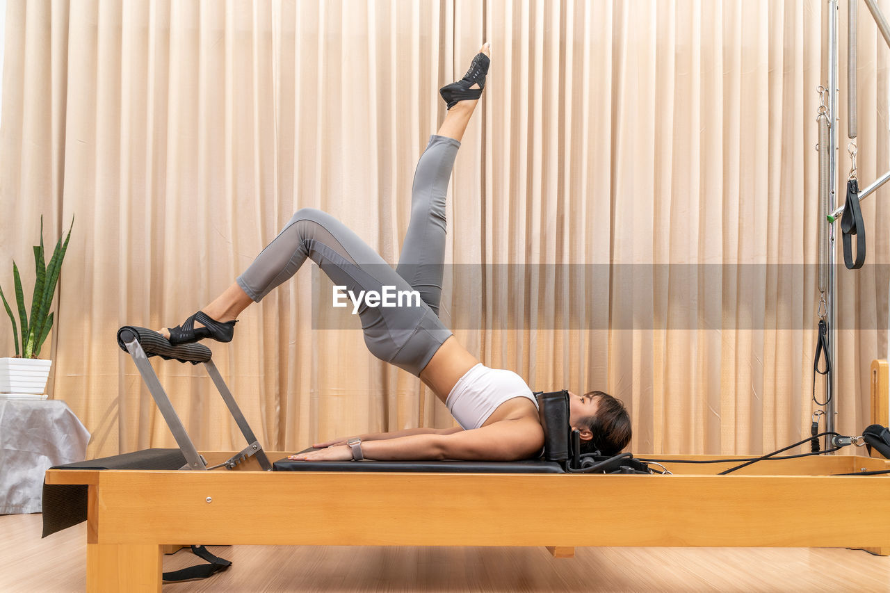 Young asian woman working on pilates reformer machine during her health exercise training