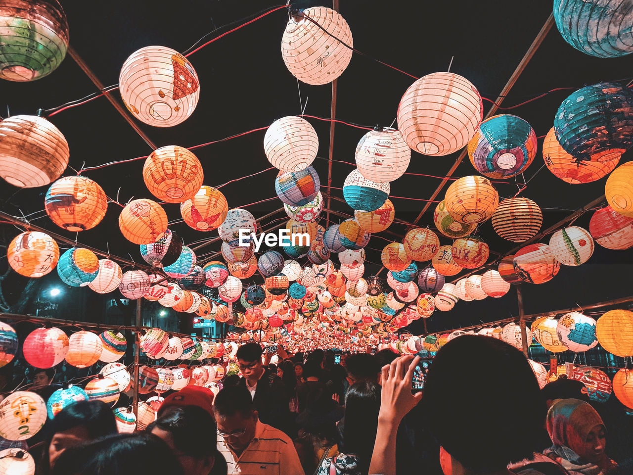 LOW ANGLE VIEW OF PEOPLE HANGING IN ILLUMINATED LANTERNS