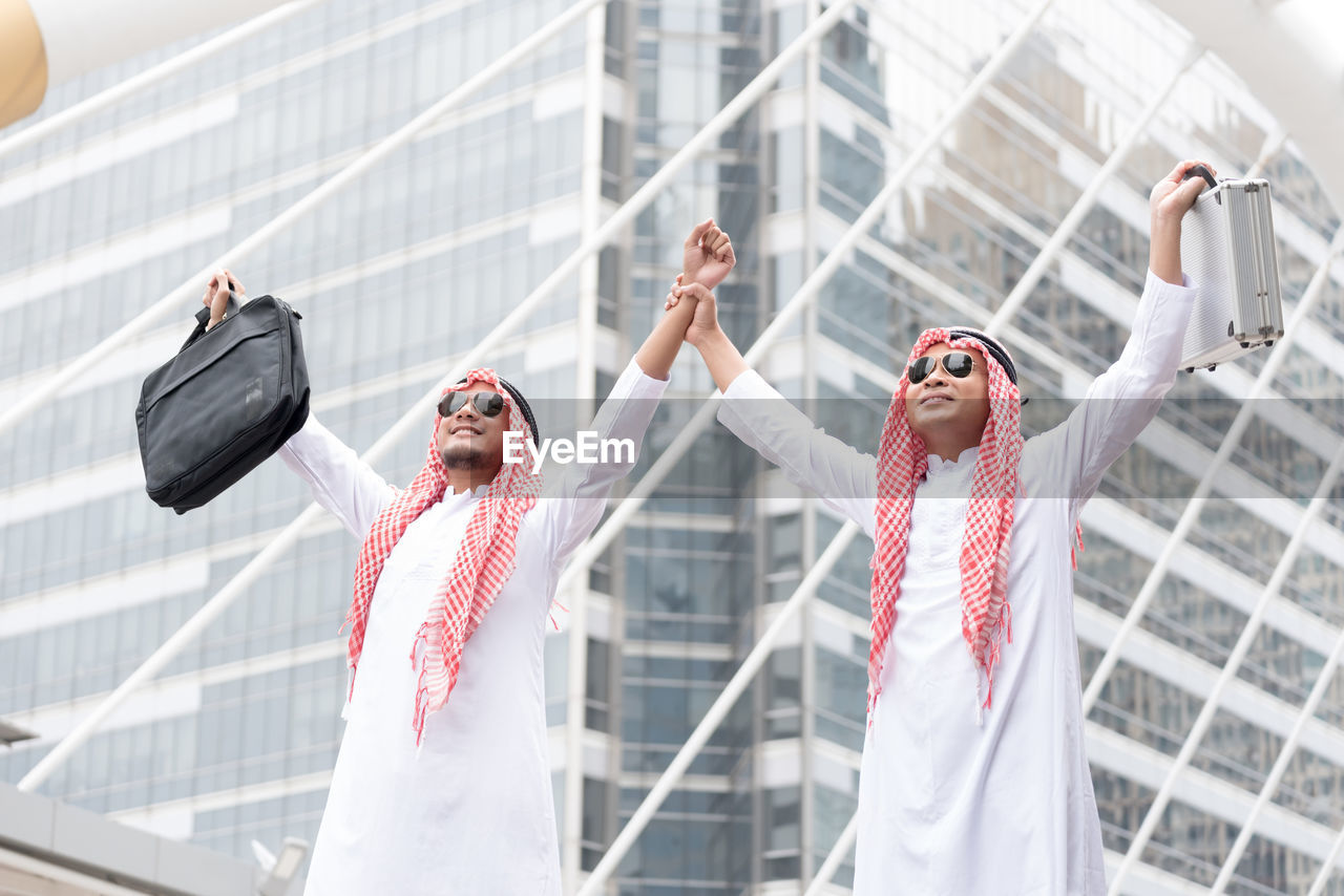 Businessmen in traditional clothing standing against skyscraper