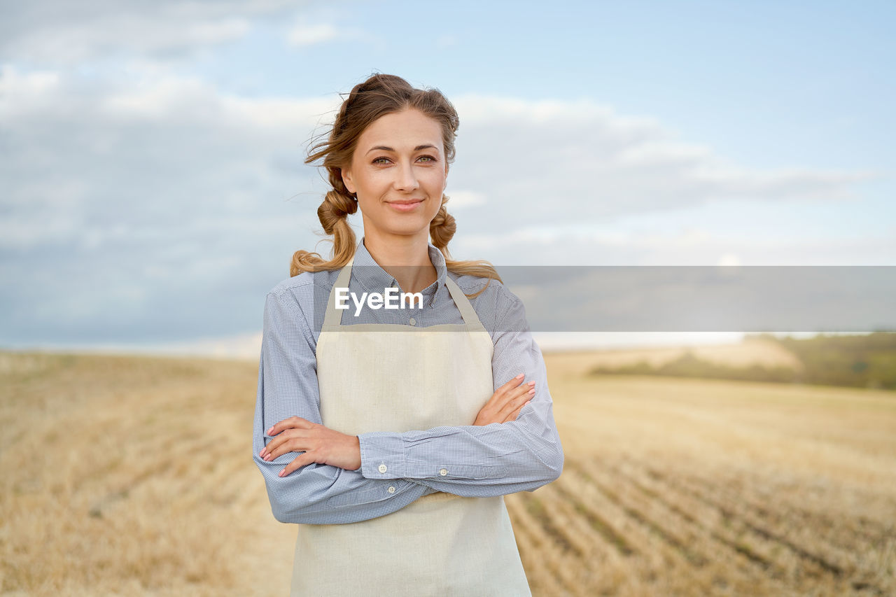 PORTRAIT OF SMILING WOMAN STANDING ON FIELD