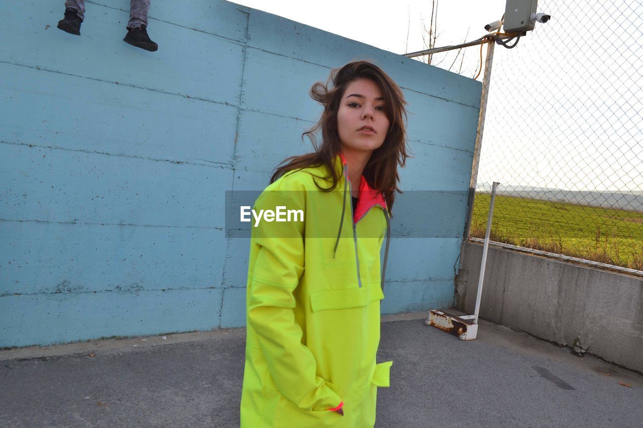 Portrait of young woman standing against wall outdoors