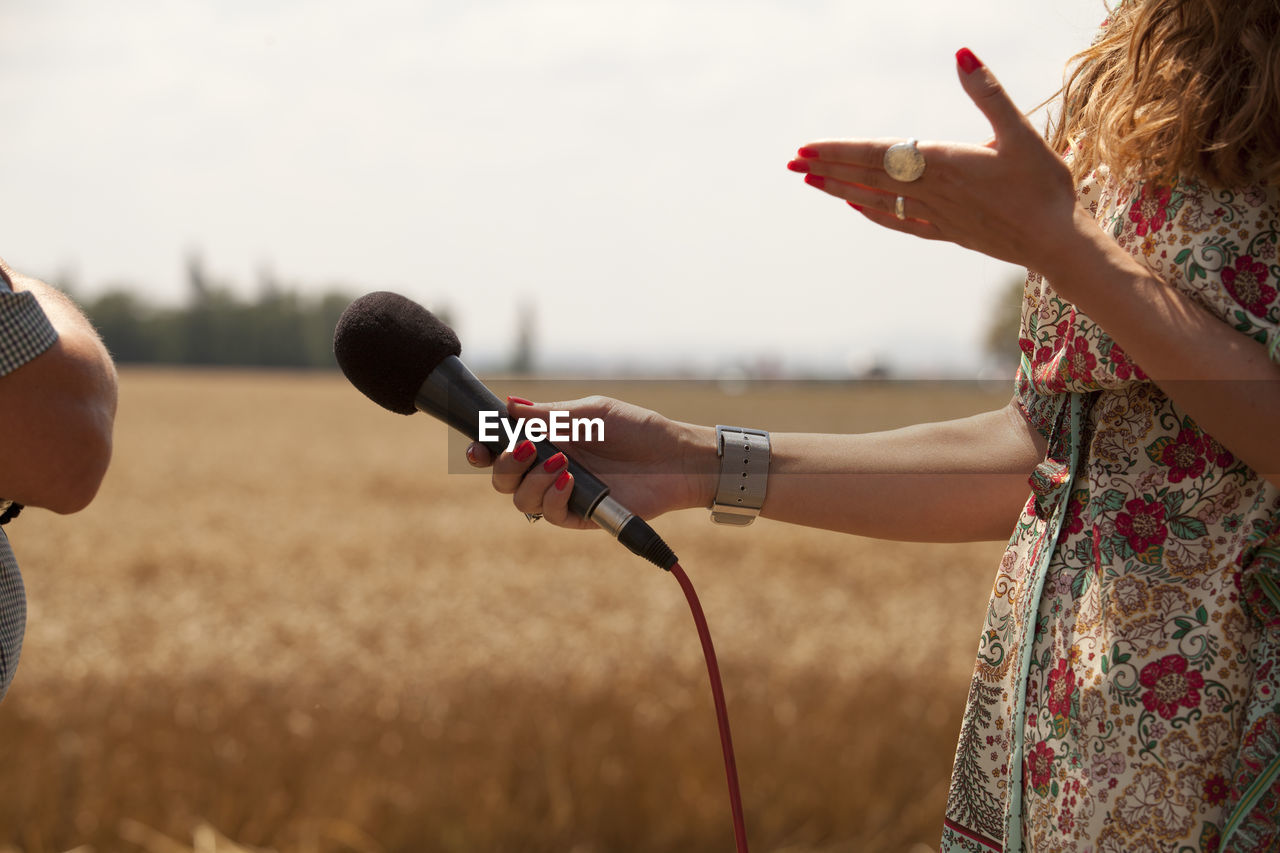 Midsection of woman holding microphone on field