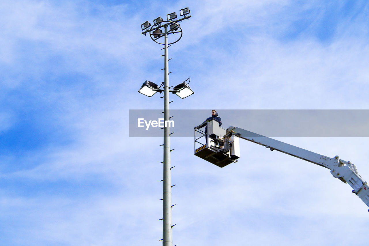 Low angle view of man standing in cherry picker against sky