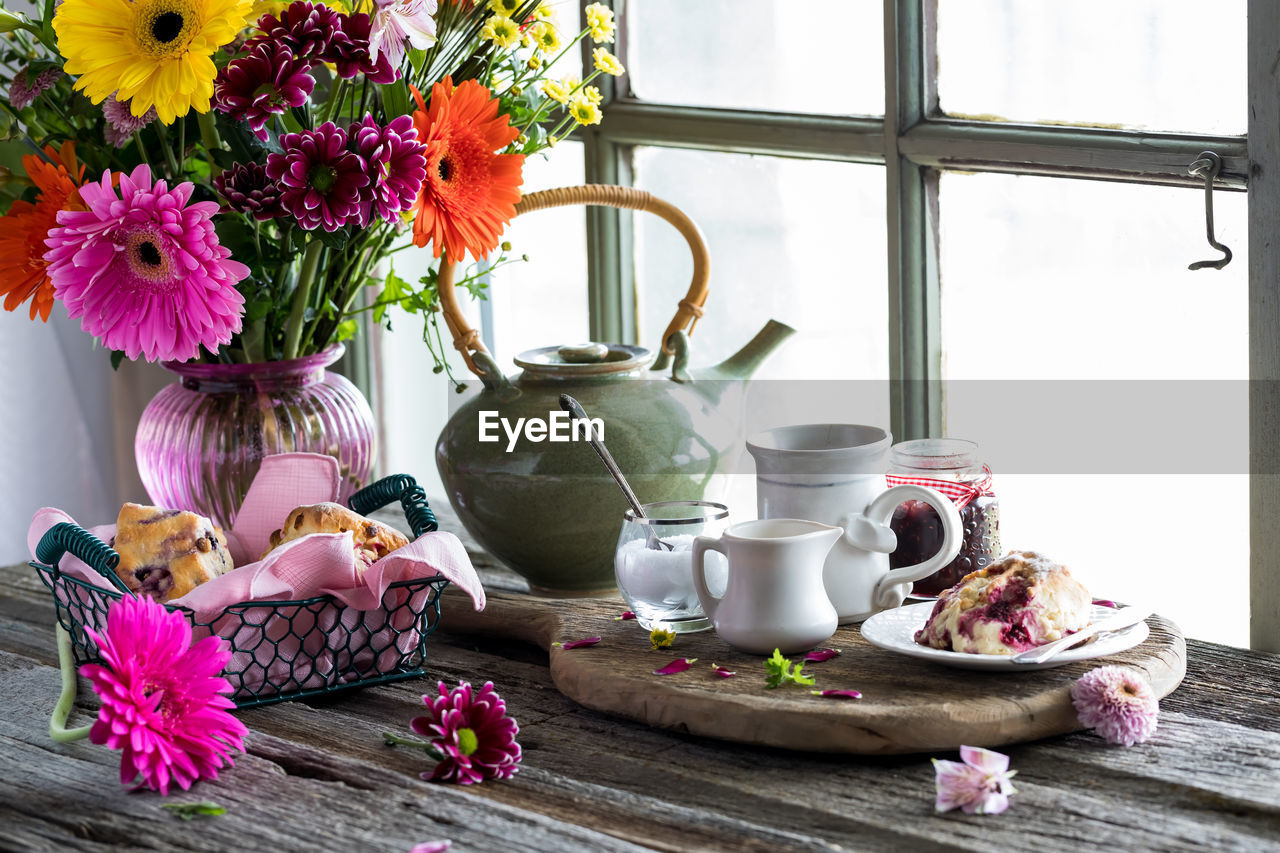 A rustic window setting of tea and scones with a vase of colourful flowers.