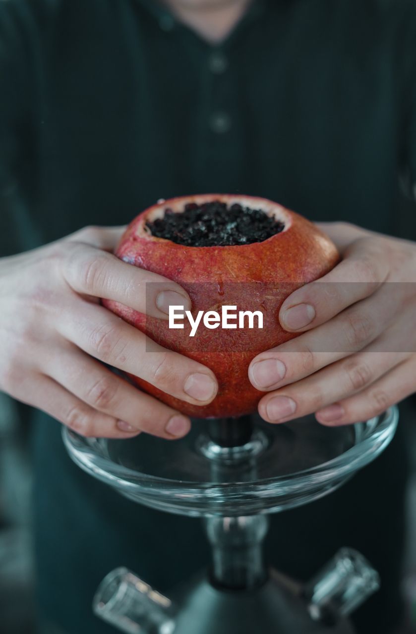 Midsection of man holding pomegranate on hookah