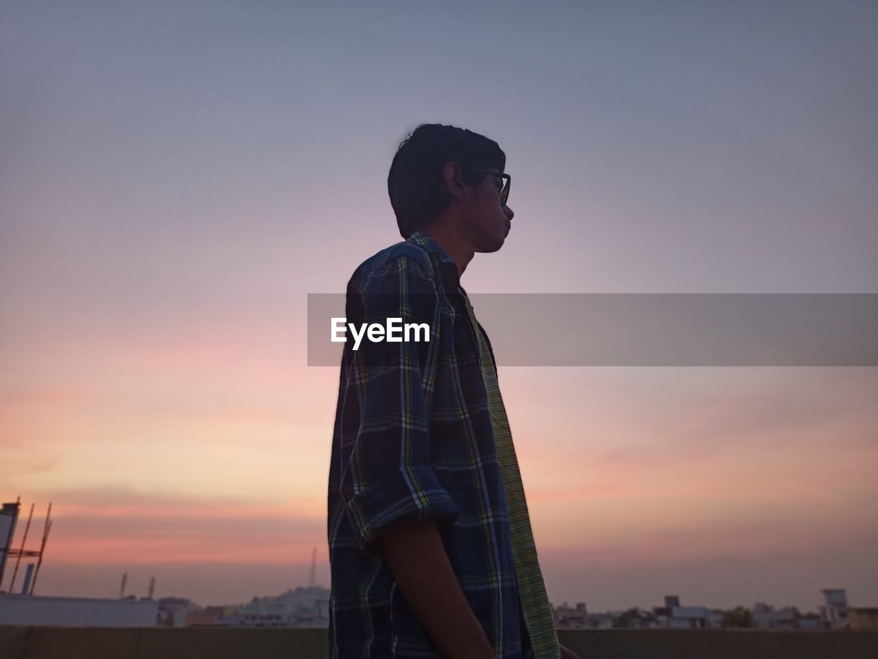 Side view of young man looking away against sky during sunset