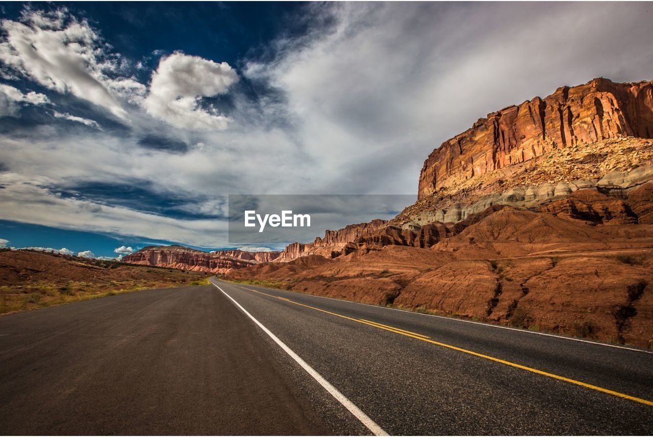 empty road leading towards mountains against sky