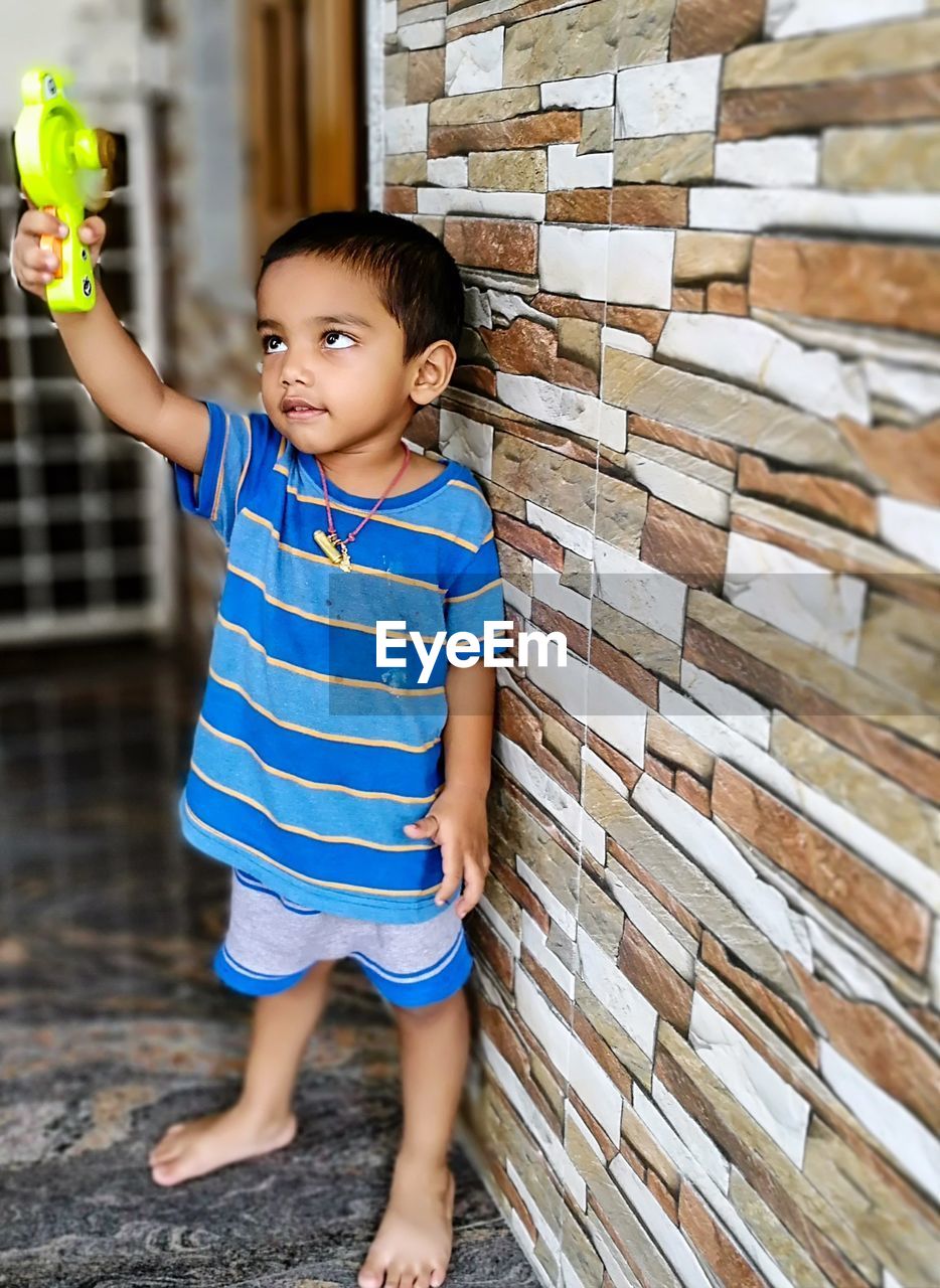 Boy playing with toy while standing against wall