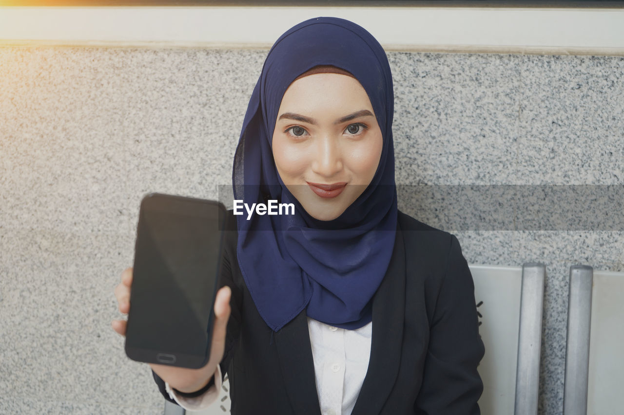 Portrait of young woman wearing hijab showing mobile phone