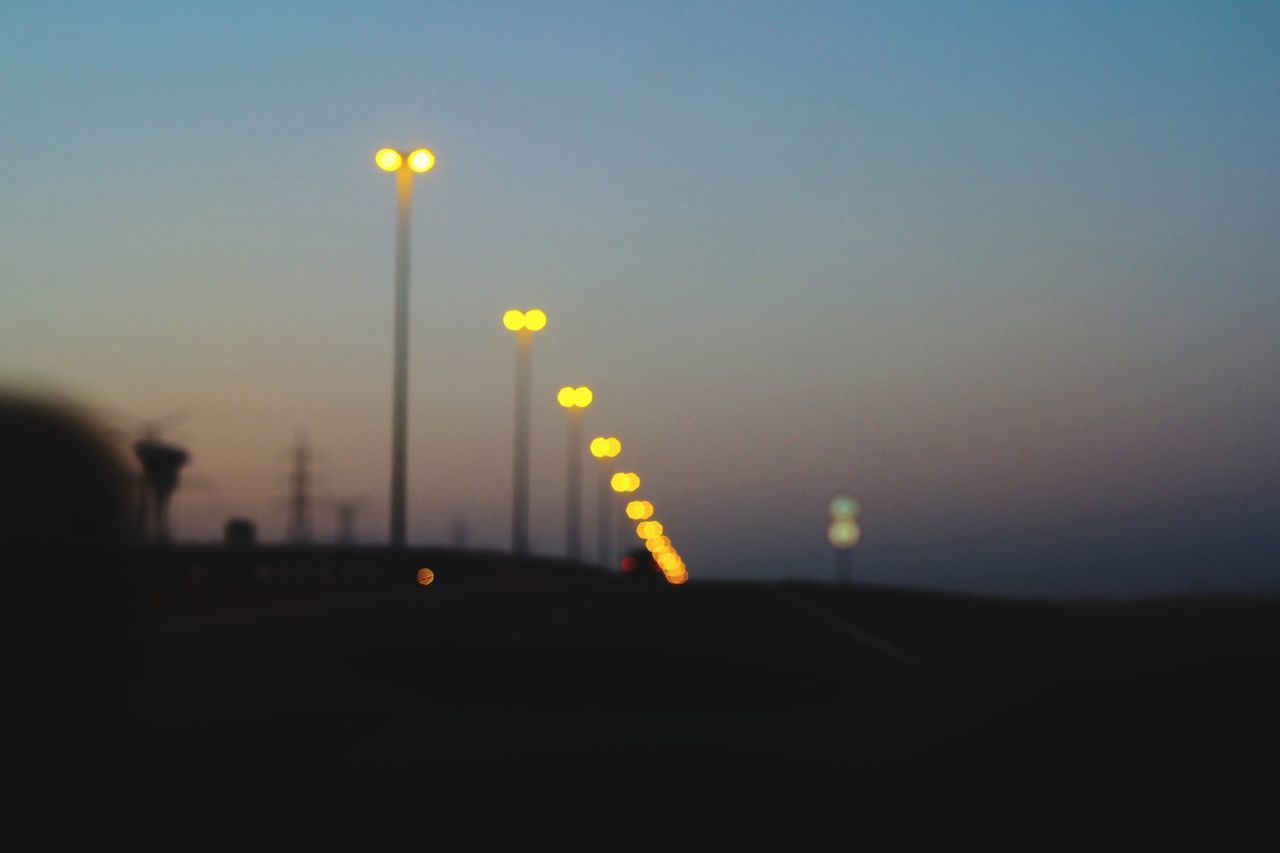 Defocused image of illuminated street lights against sky during sunset