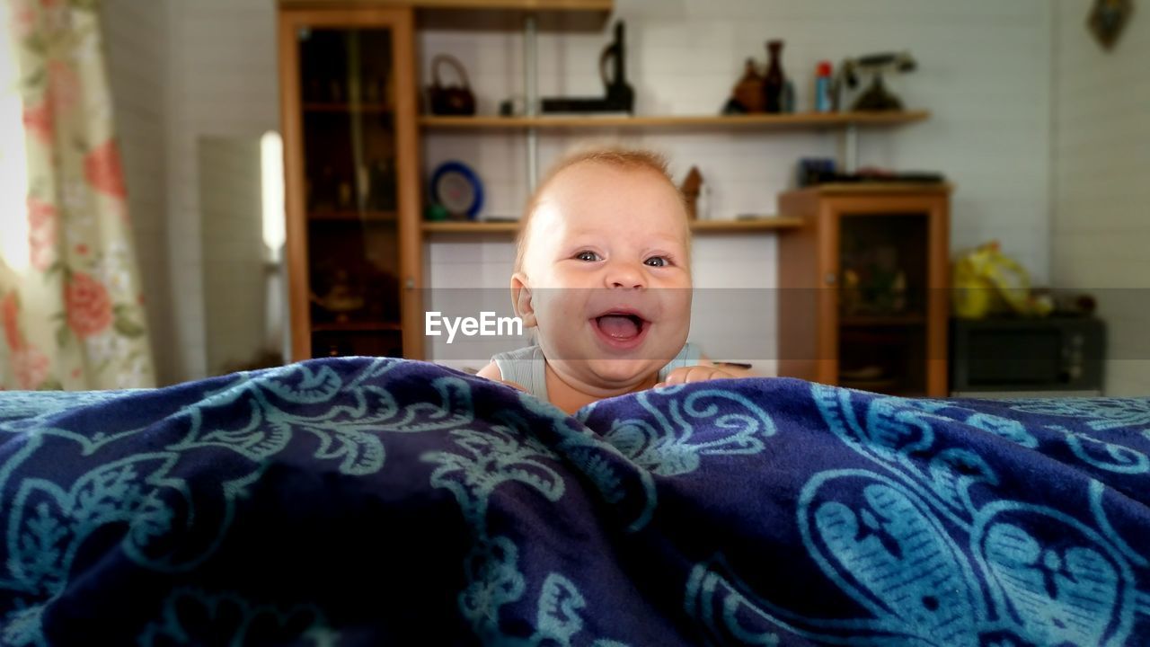 Portrait of cheerful baby boy on bed at home