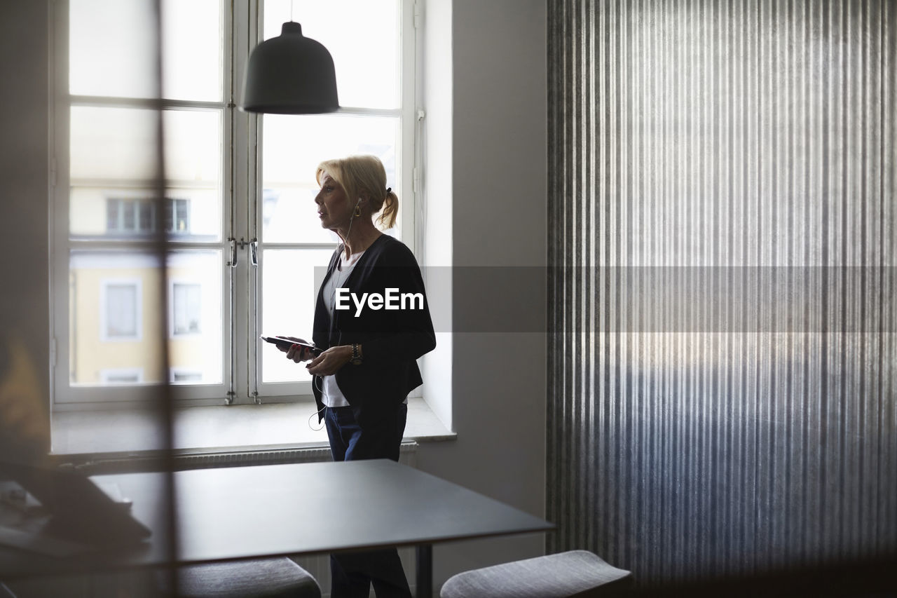 Senior businesswoman using mobile phone against window at creative office