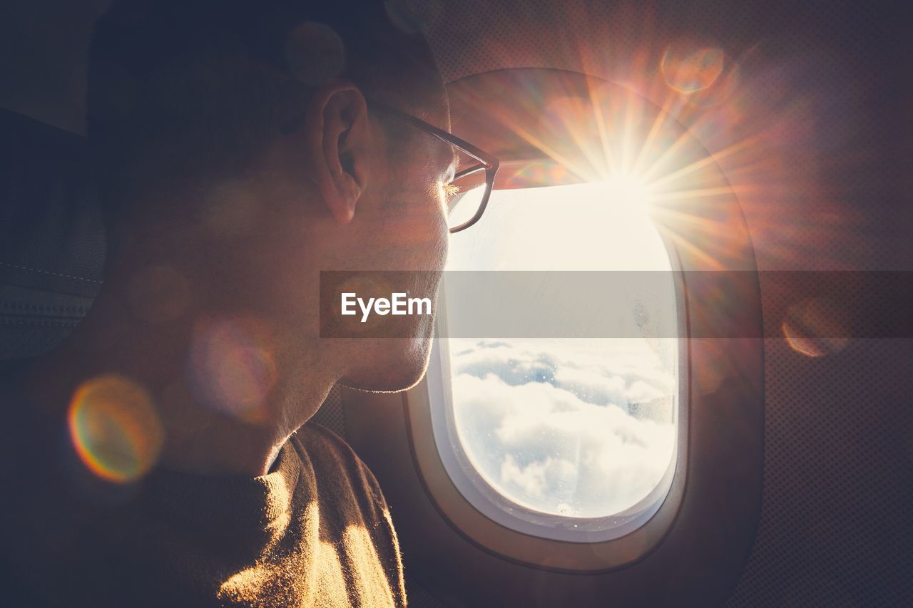 Man looking through airplane window during sunny day