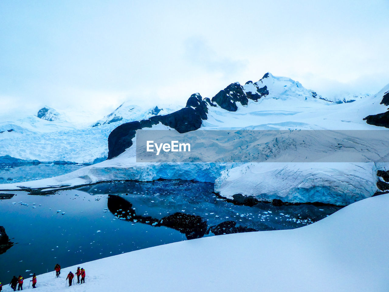 Group of hikers in snowy landscape with mountains and sea in antarctica 