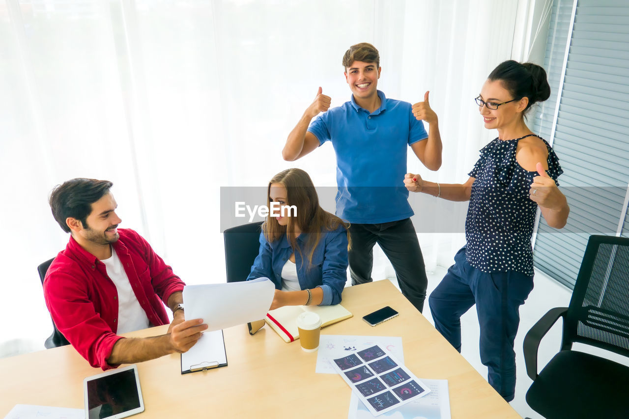 YOUNG COUPLE STANDING ON TABLE IN OFFICE