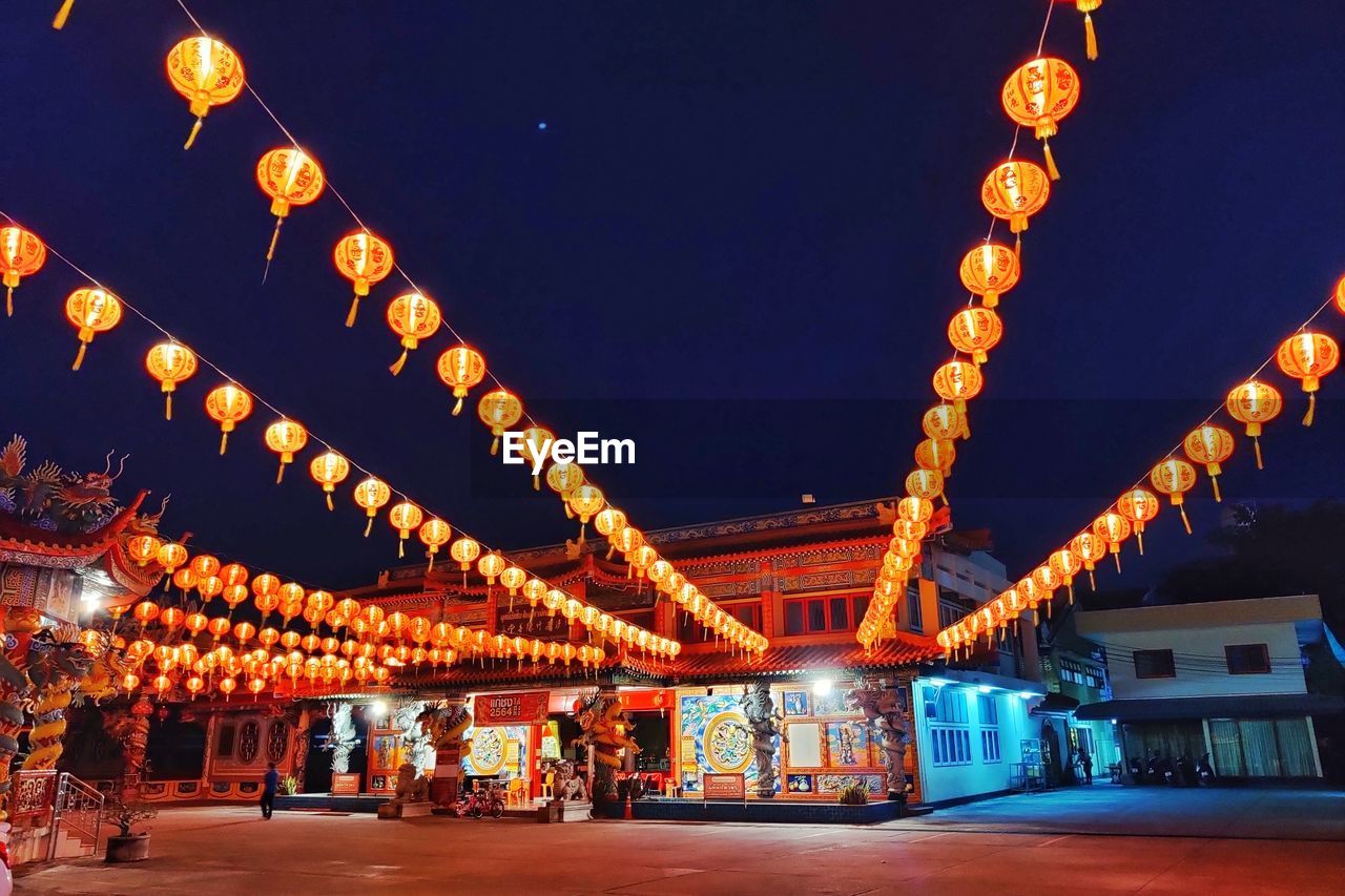 Illuminated lanterns hanging by chinese building against sky at night