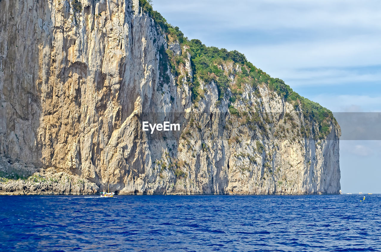 Scenic view of sea by mountain against sky