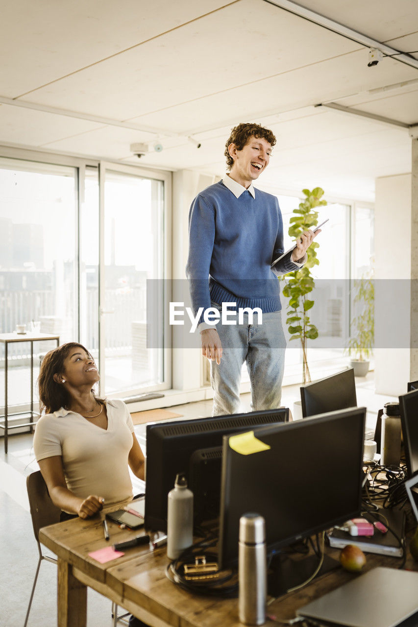 Happy entrepreneur standing on chair by colleague at desk in creative office