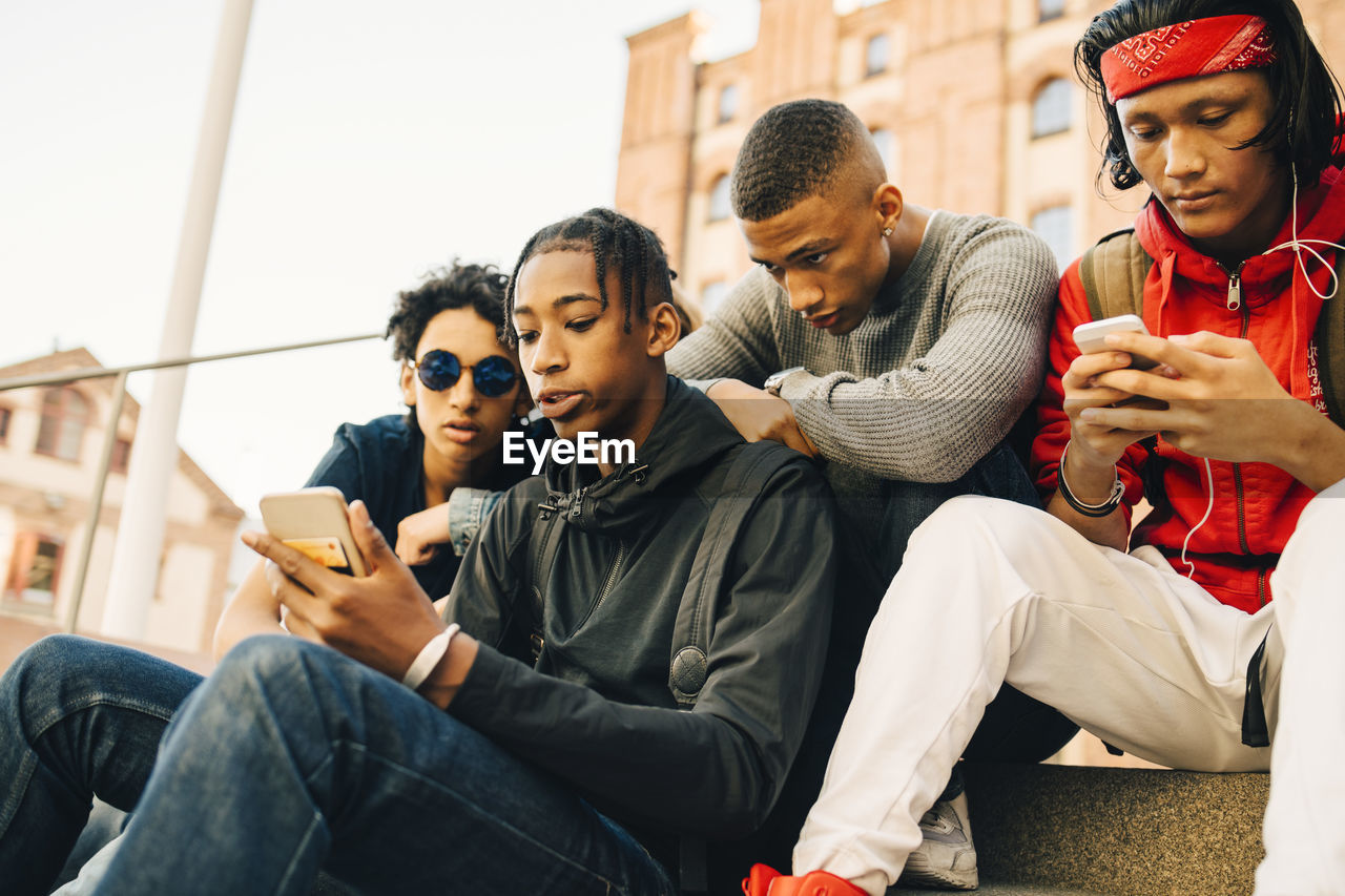 Male friends using mobile phones while sitting in city