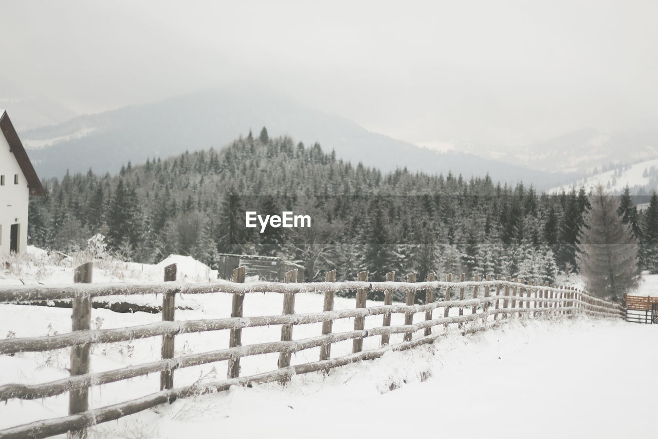 Snow covered fence on landscape against sky