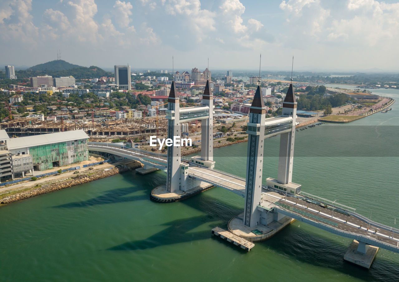 HIGH ANGLE VIEW OF BUILDINGS AND RIVER AGAINST SKY