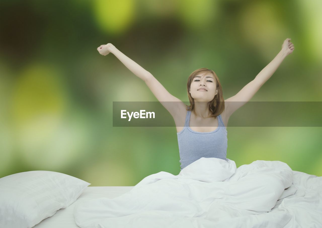 Woman stretching hands on bed against trees