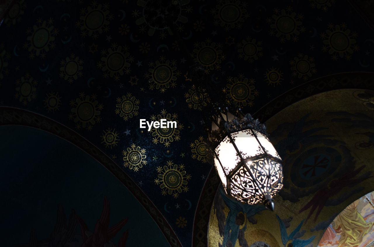 LOW ANGLE VIEW OF ILLUMINATED CHANDELIER HANGING ON CEILING IN BUILDING