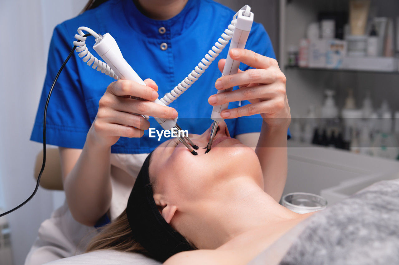 Close-up of a professional cosmetologist's hands touching a woman's cheek with equipment. young