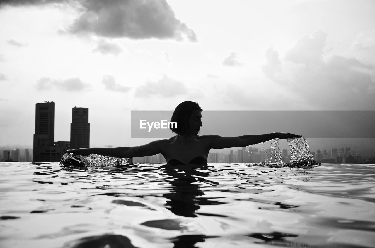 WOMAN IN SWIMMING POOL AGAINST SKY