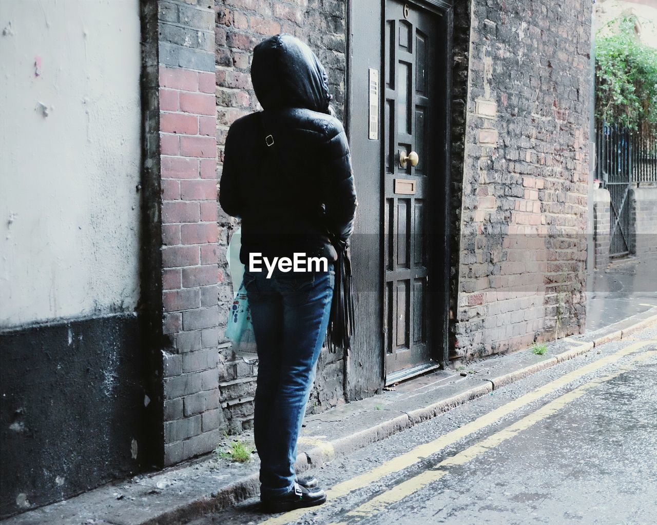 Rear view of hooded person standing on street by old building