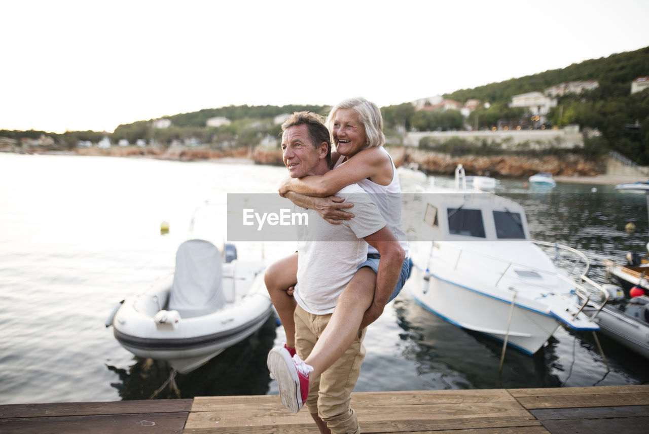 Senior man giving his wife a piggyback ride on a jetty
