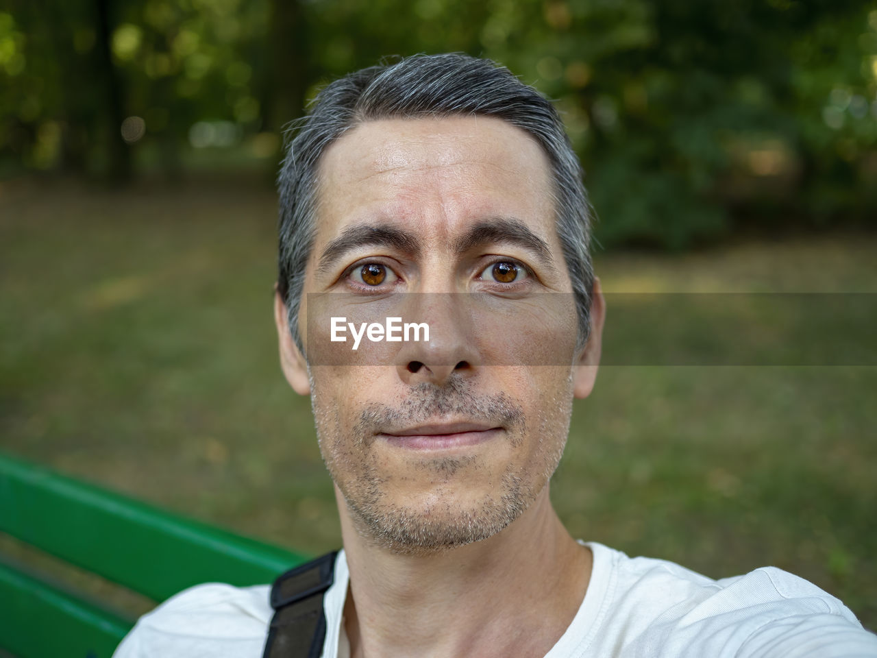 Mid age adult make selfie on the park bench during summer day. he is looking at the camera