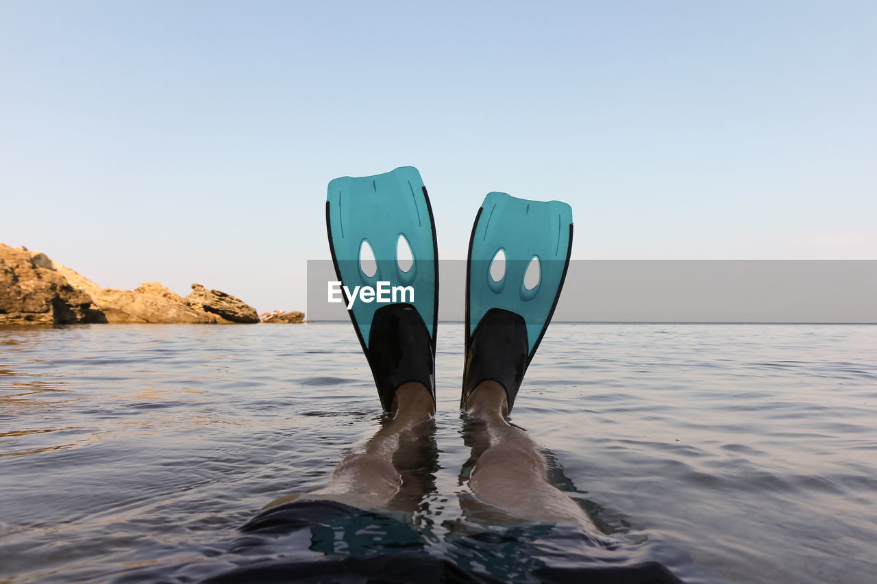 Low section of man wearing diving flippers in sea against clear sky