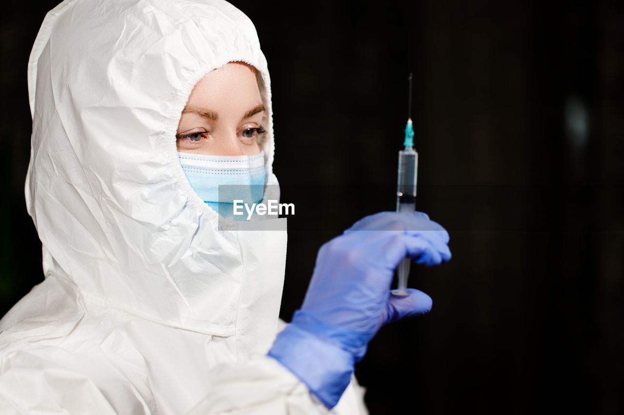 Doctor holding syringe against black background