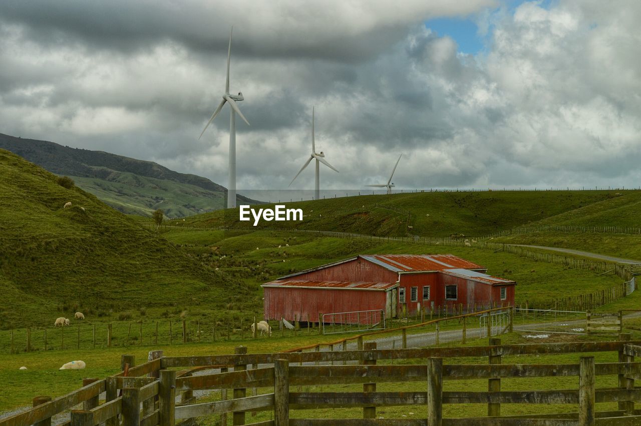 Wind turbines in field against cloudy sky