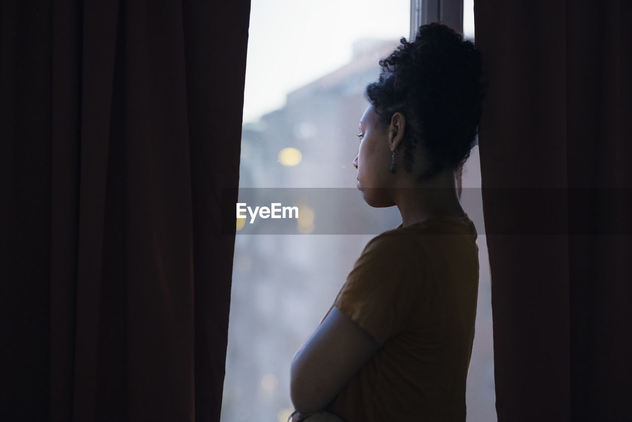 Pensive young woman looking through window