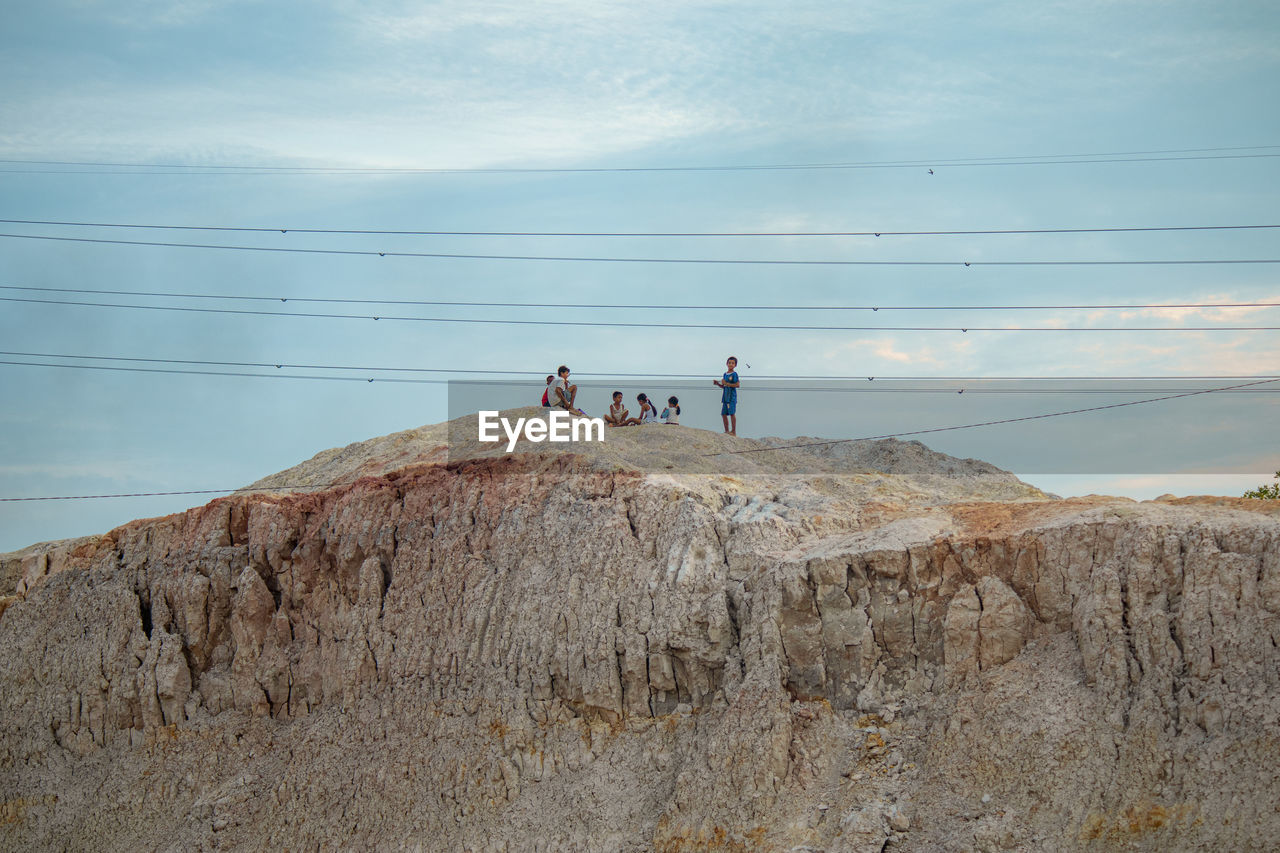 Children on rocks by mountain against sky