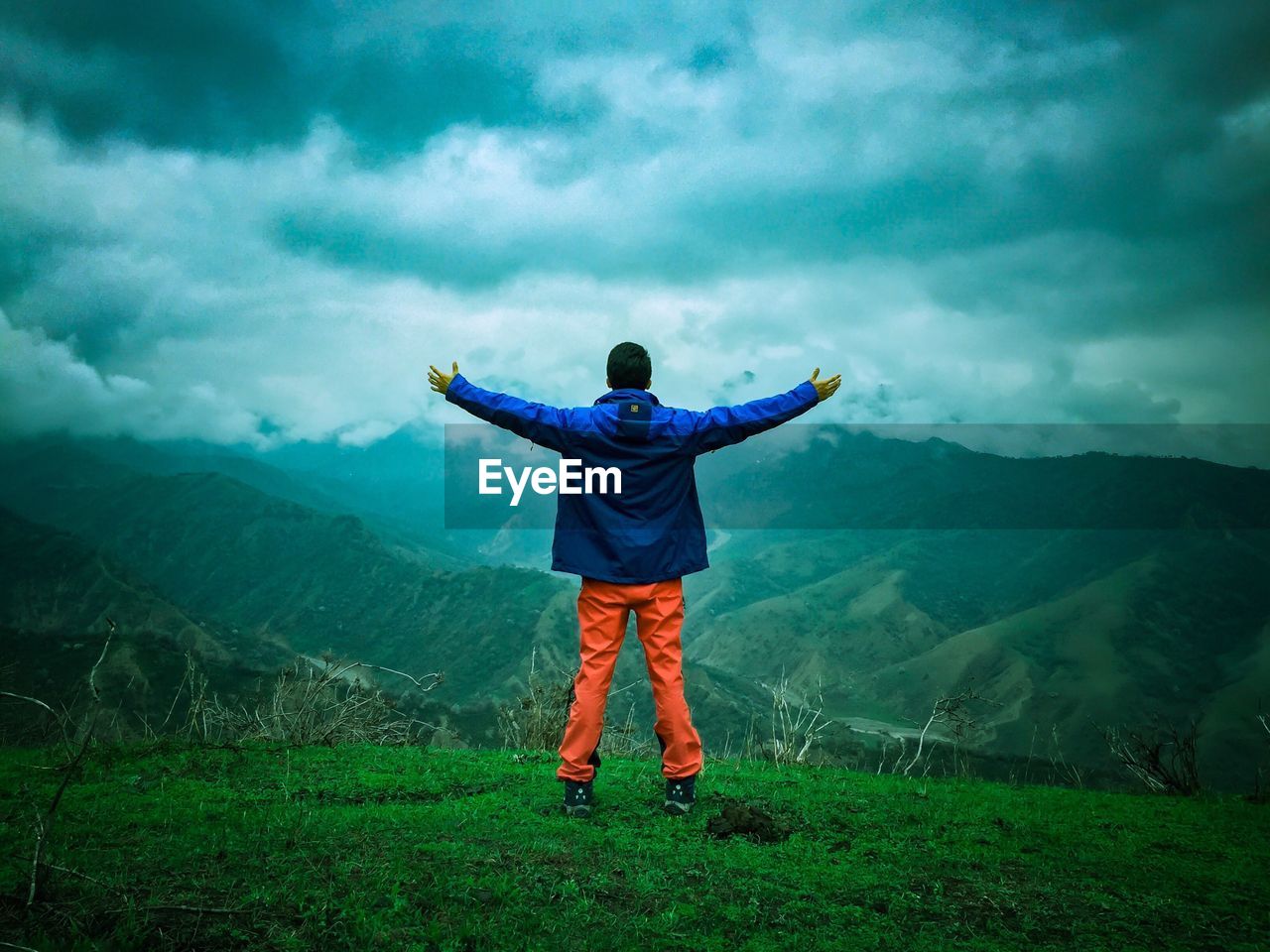 Rear view of man with arms outstretched standing on mountain against cloudy sky