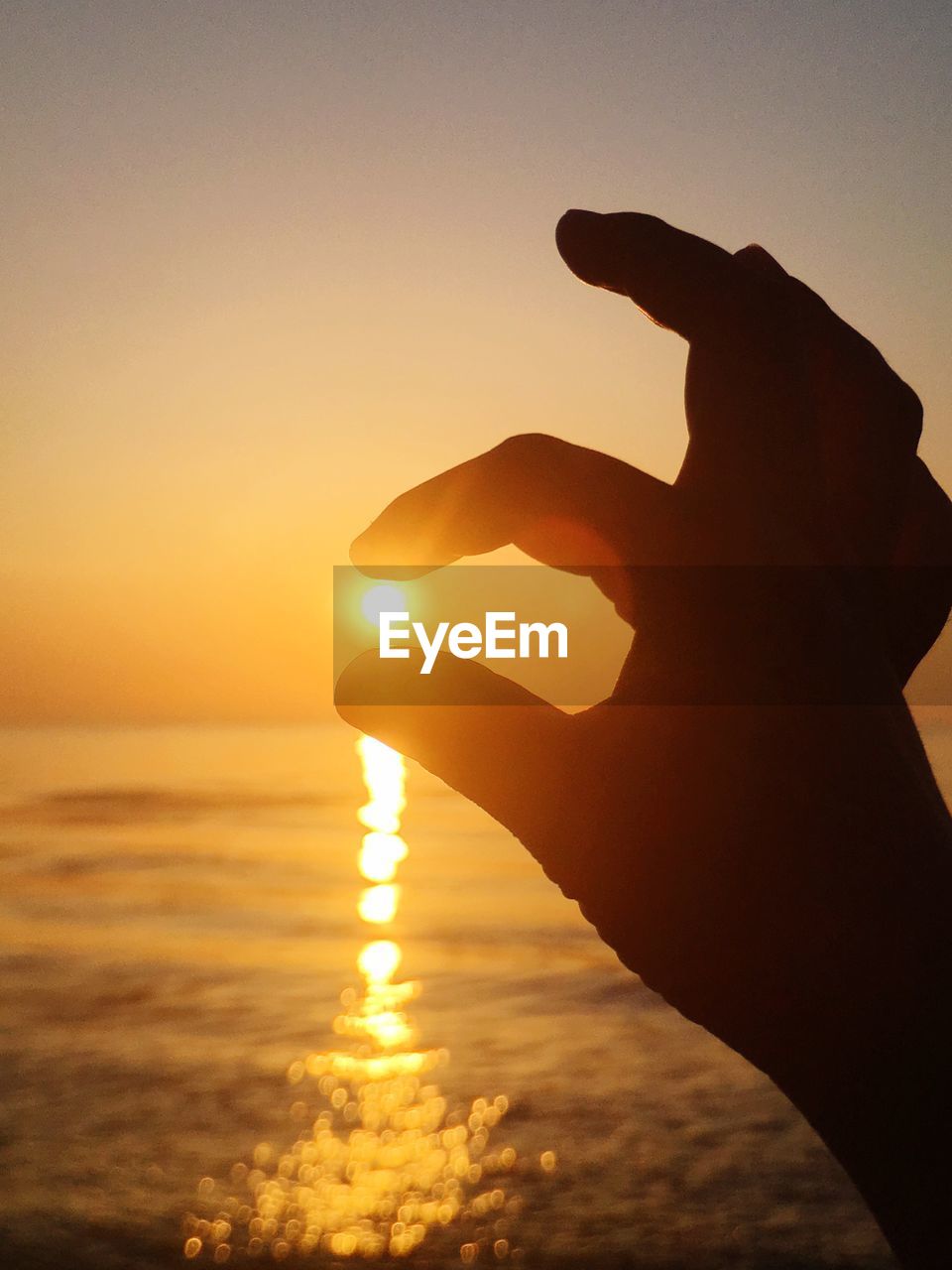 Optical illusion of hand holding sun at beach