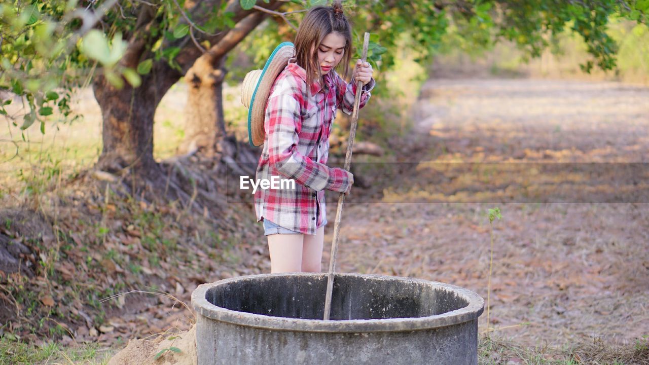 Young woman putting pole in well at farm