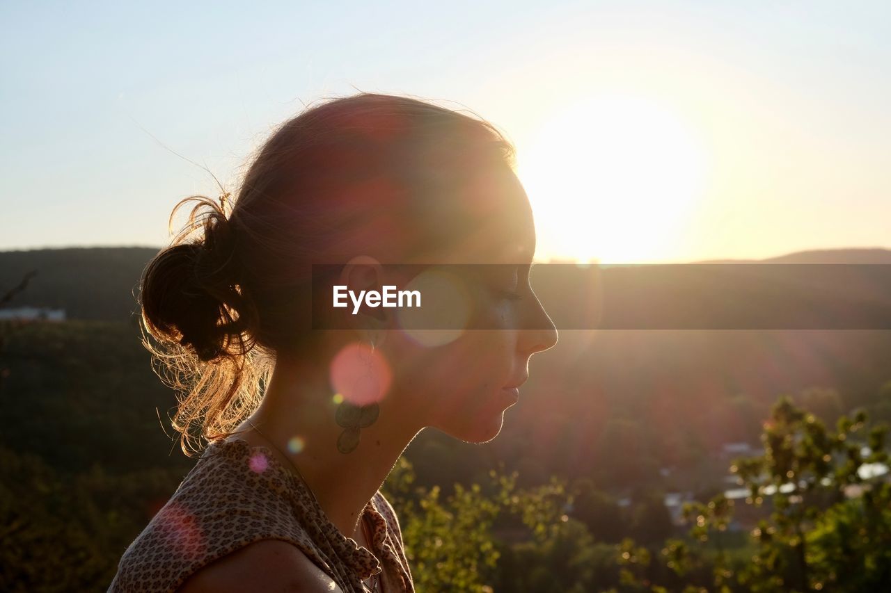 Close-up of woman with eyes closed against sky during sunset