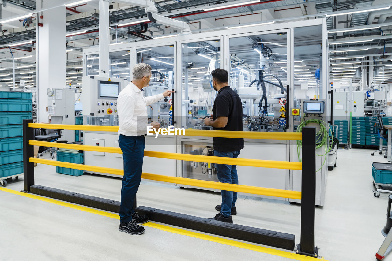 Businessman pointing at machine with engineer in factory