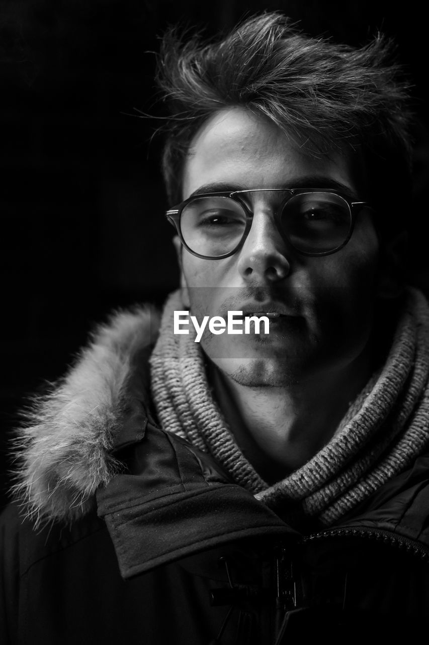 Portrait of young man wearing eyeglasses against black background